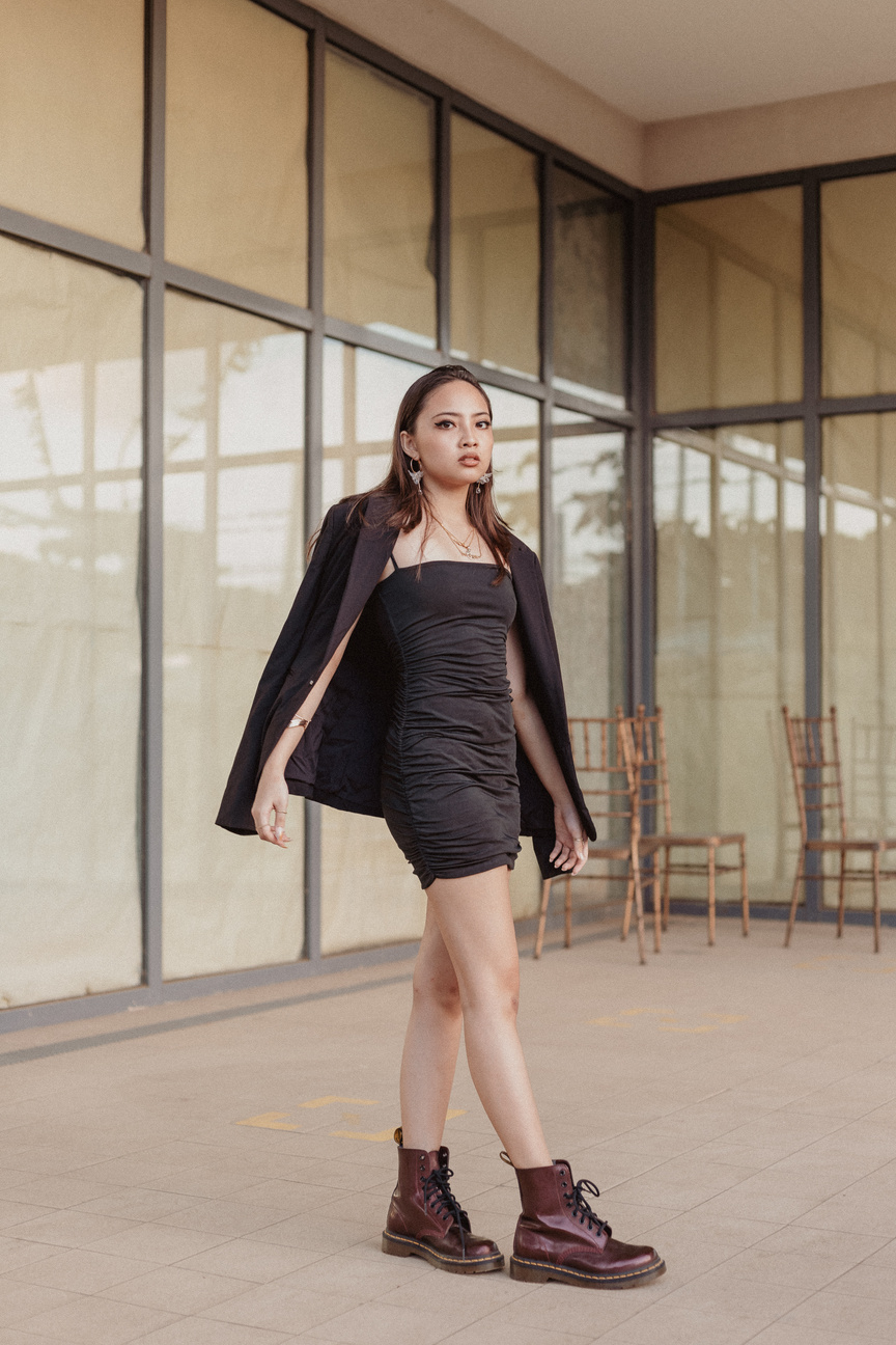 a person in a black dress and jacket standing in front of a building